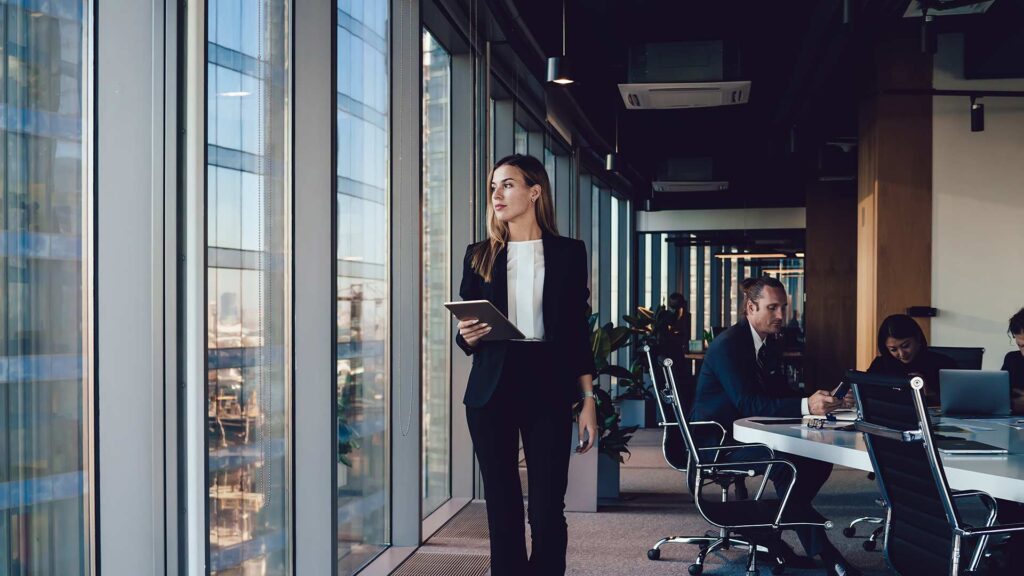 A professional woman in a sharp suit looking out the window of a boardroom