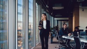A professional woman in a sharp suit looking out the window of a boardroom